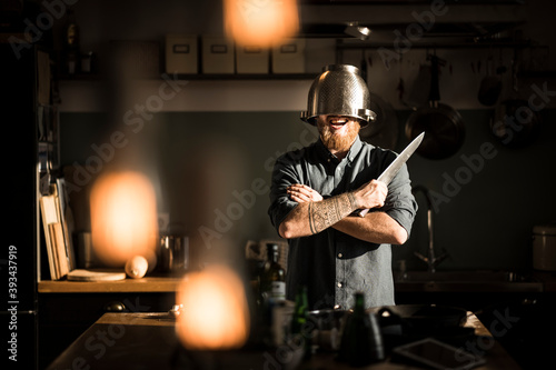 Man with kitchen knife standing in kitchen, wearing colander as helmet photo