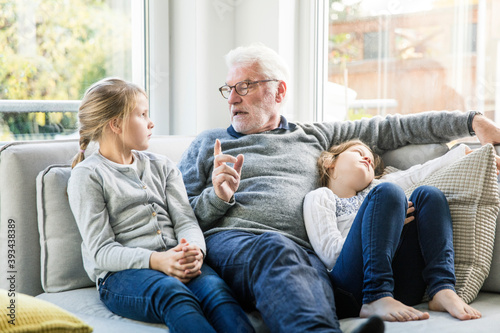 Grandfather talking to two girls on sofa in living room photo