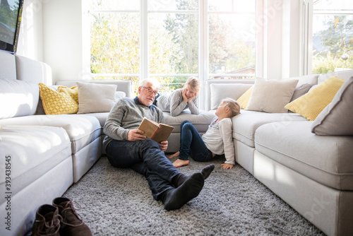 Two girls and grandfather reading book in living room photo