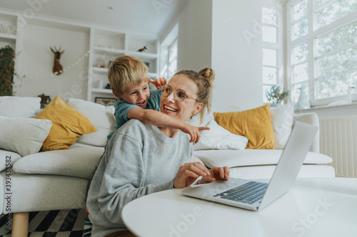 Boy pointing at laptop while standing behind mother at home photo