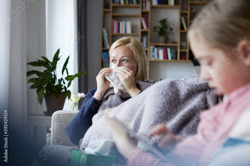 Mother sitting on couch, having a cold, daughter playing in foreground