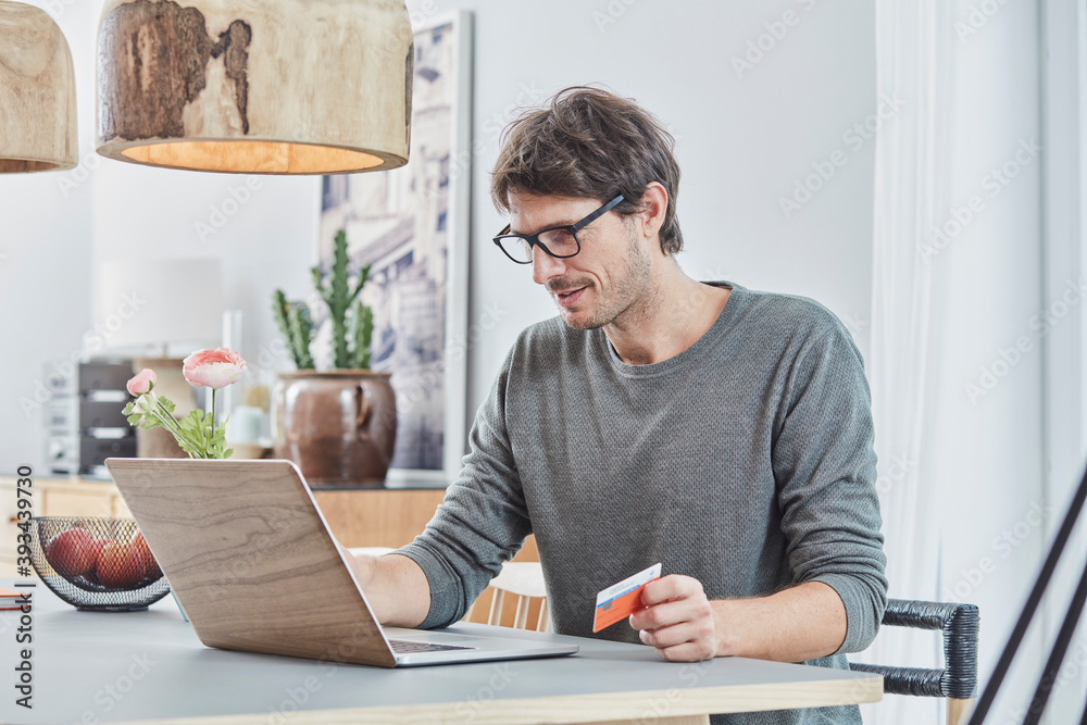 Man holding a card using laptop on table at home Man holding a card using laptop on table at home
