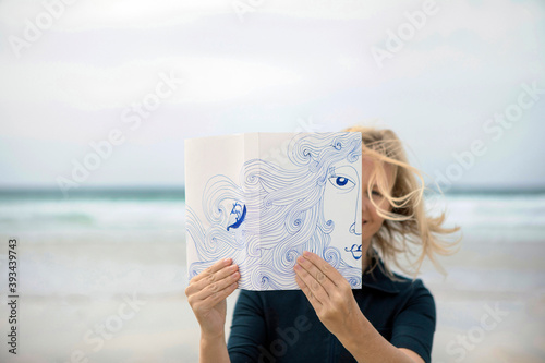 Woman covering face with book, reading poetry on beach photo