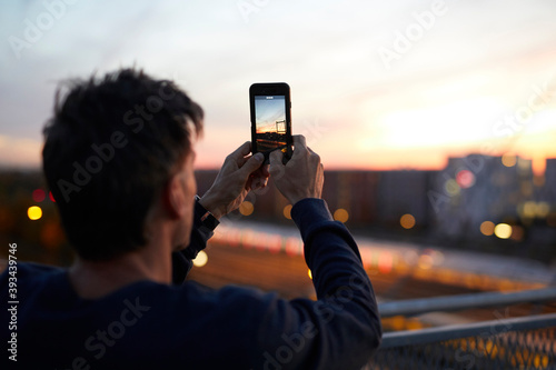 Man in the city taking cell phone picture in the evening photo