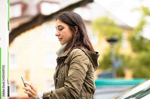 Beautiful woman using smart phone for renting electric car at charging station