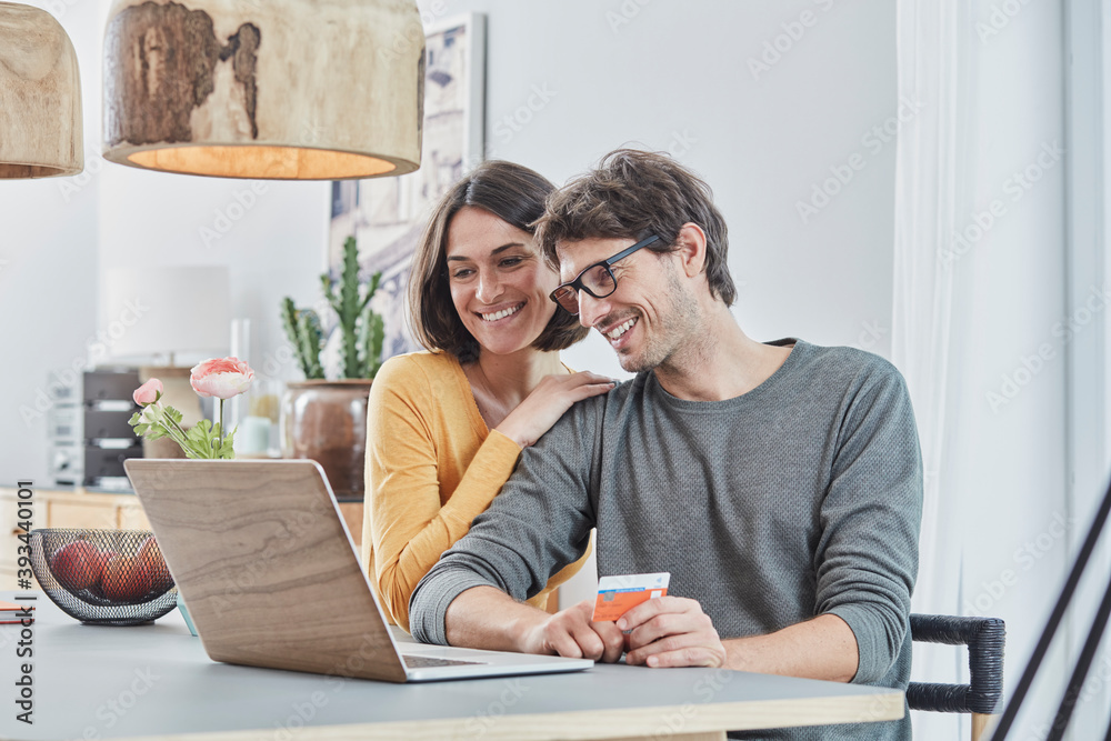 Happy couple with a card using laptop on table at home