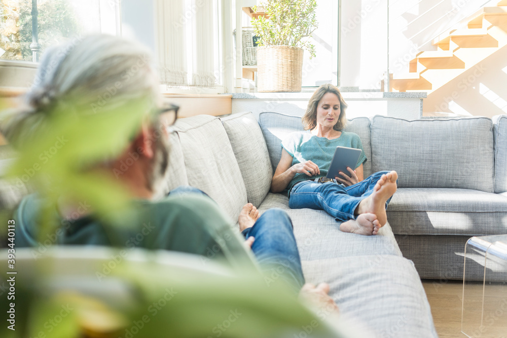 Mature couple relaxing on couch at home with woman holding tablet Mature couple relaxing on couch at home with woman holding tablet