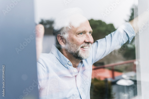 Portrait of happy mature man looking out of windowpane