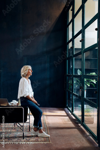 Casual mature businesswoman looking out of window in loft office photo