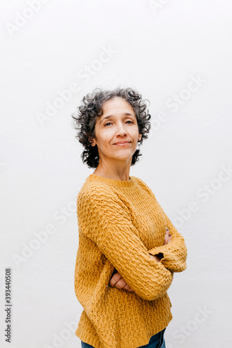 Confident woman wearing sweater while standing with arms crossed against white wall