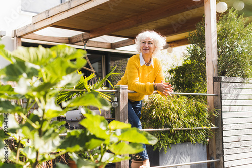 Smiling woman leaning on railing while looking away standing at home in balcony photo