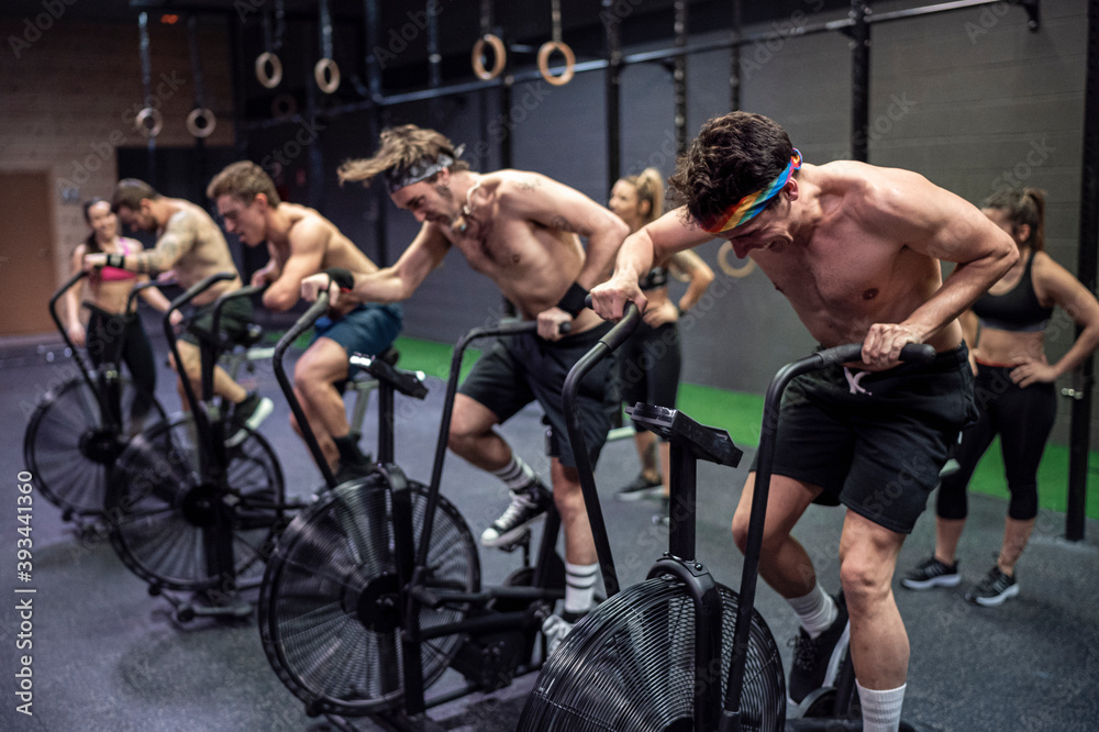 Athletes cycling on exercise bike with women standing in background at gym Athletes cycling on exercise bike with women standing in background at gym