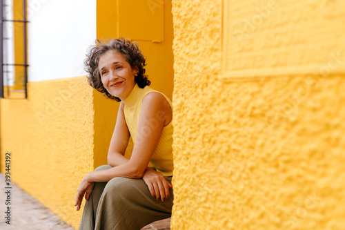Happy mature woman sitting on doorway against wall