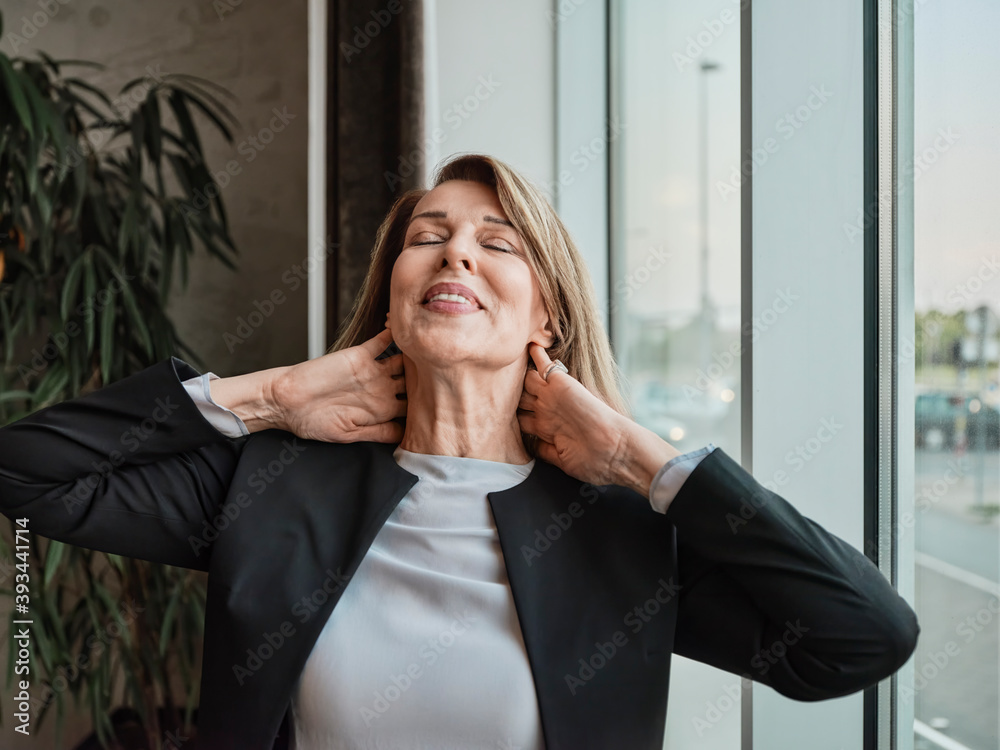 Senior woman with hands behind head standing in hotel lobby Senior woman with hands behind head standing in hotel lobby