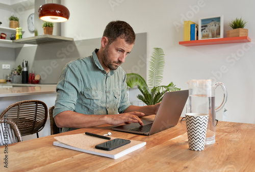 Handsome male freelancer using laptop at dining table while working from home
