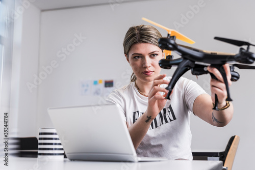 Young woman with laptop at desk holding drone photo