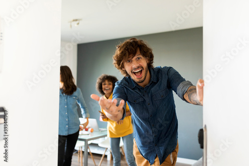 Portrait of surprised man with friends in background opening the door