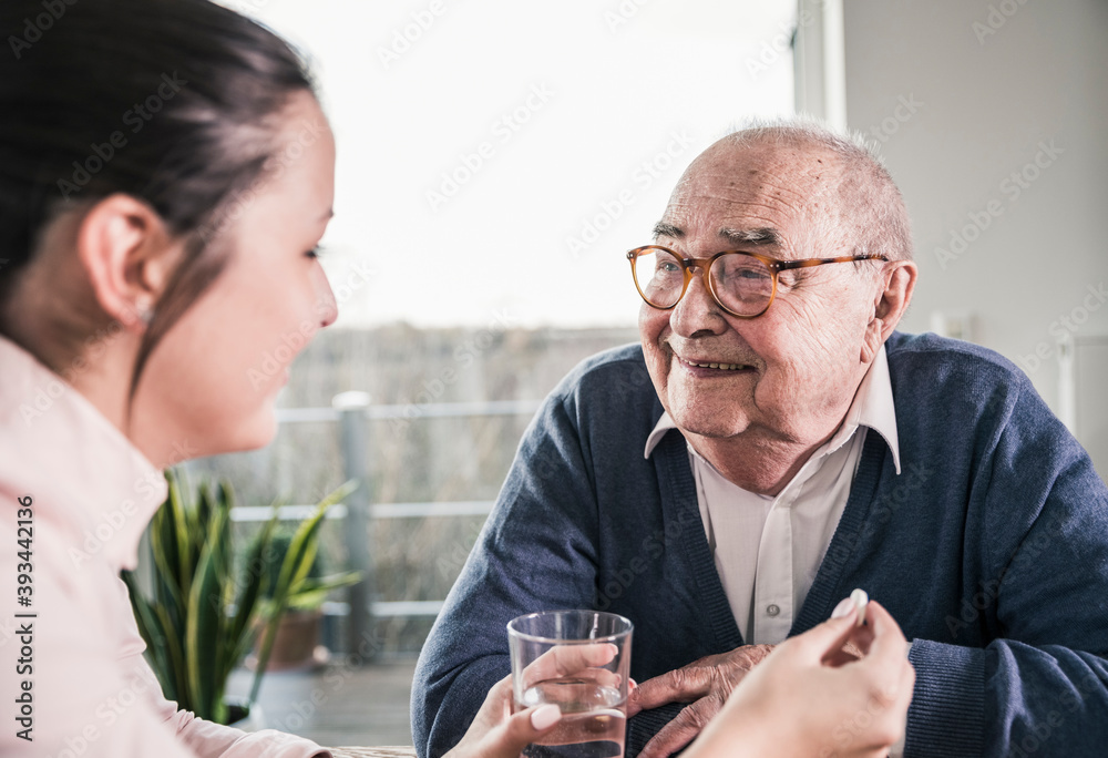 Woman holding pill and glass of water for smiling senior man Woman holding pill and glass of water for smiling senior man
