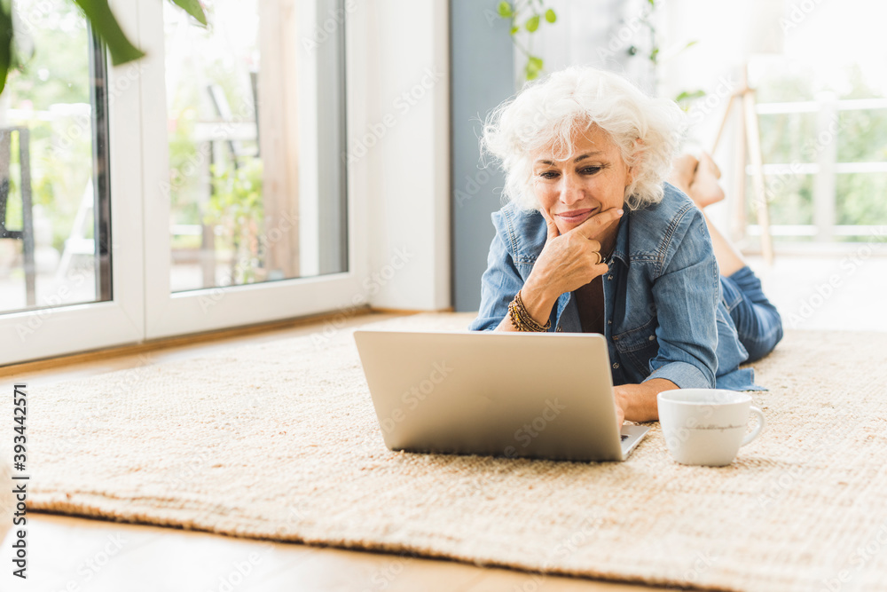 Mature woman lying on front while working on laptop at home
