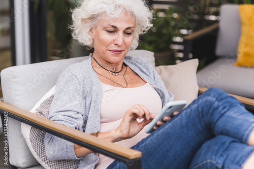 Mature woman texting messaging while sitting on couch at home