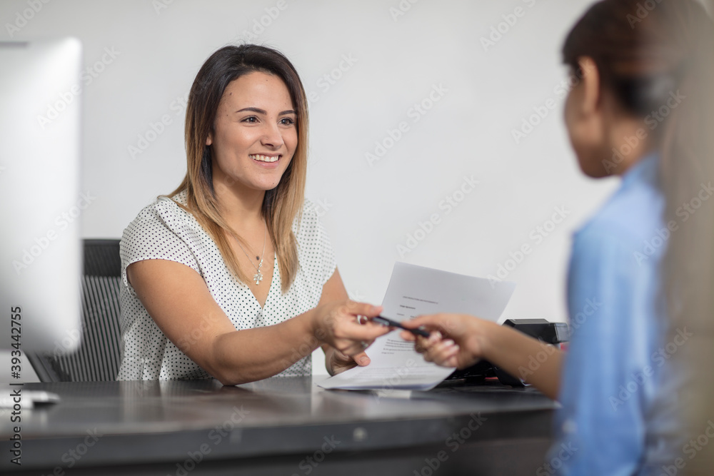 Smiling woman handing over pen to client at desk Smiling woman handing over pen to client at desk