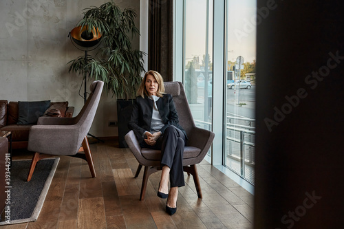 Serious senior woman sitting on chair in hotel lobby photo