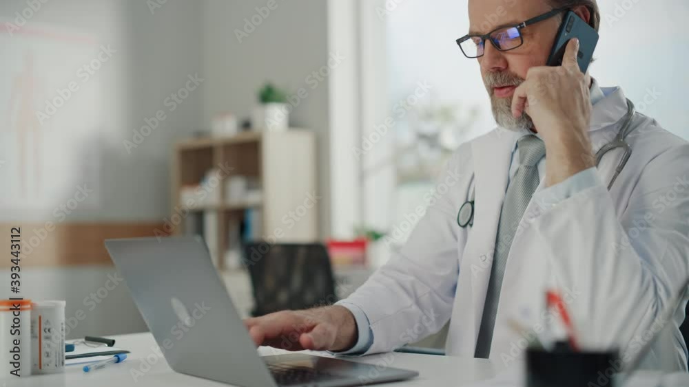 Doctor's Consultation Office: Experienced Physician Working on a Laptop, Takes a Call from the Patient, Talks about Test Results, and Prescribes Medicine. Health Care Specialist Planning Treatment Doctor's Consultation Office: Experienced Physician Working on a Laptop, Takes a Call from the Patient, Talks about Test Results, and Prescribes Medicine. Health Care Specialist Planning Treatment