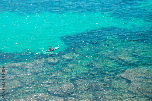 Aerial view of people paddling on SUP (stand up paddle) on crystal clear blue sea with rocks under water. Unidentifiable people paddle boarding.