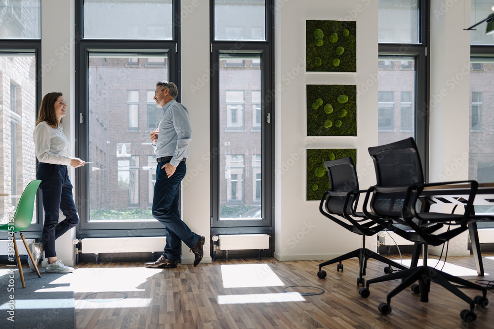 Man and woman talking while leaning on wall at office Man and woman talking while leaning on wall at office