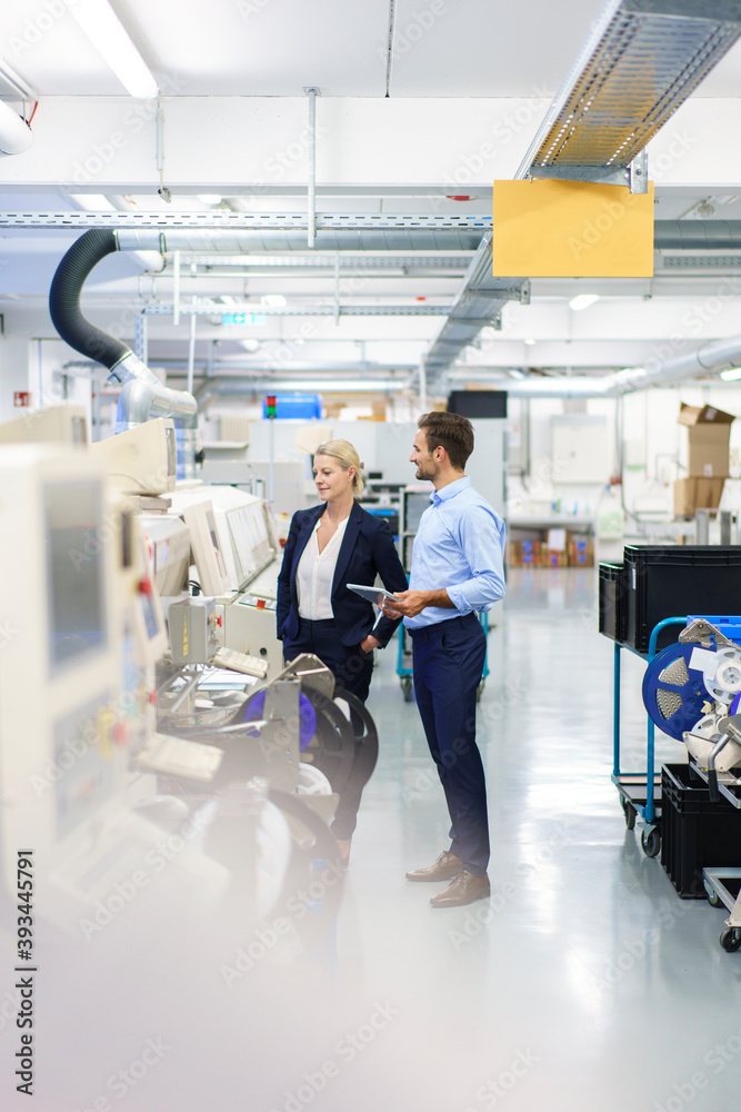 Young engineer discussing with mature businesswoman while standing by machinery at factory Young engineer discussing with mature businesswoman while standing by machinery at factory