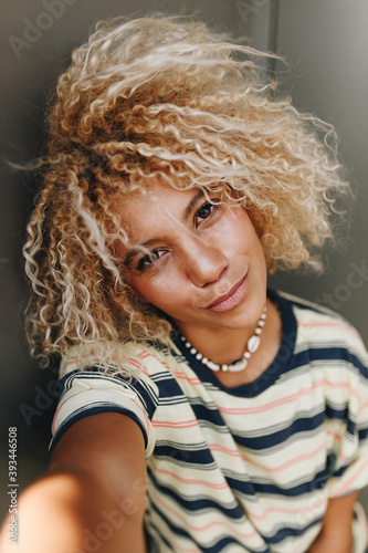 Woman with blond curly hair taking selfie against metallic wall