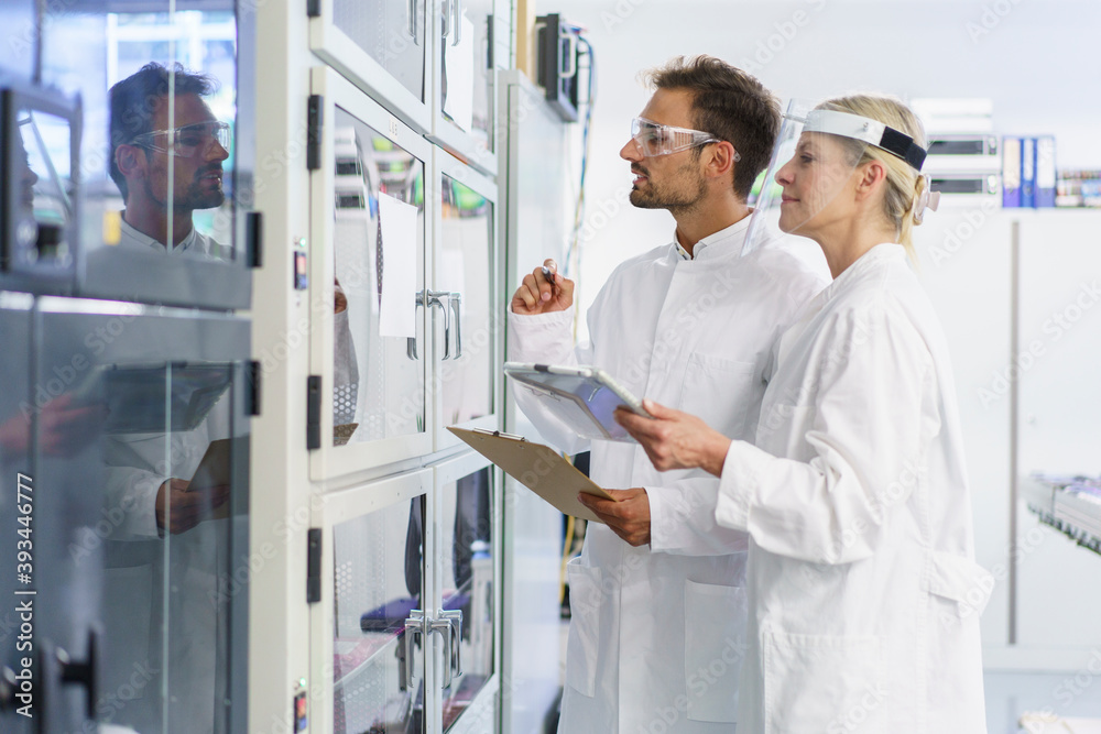 Young male technician analyzing while standing by female colleague at illuminated laboratory Young male technician analyzing while standing by female colleague at illuminated laboratory
