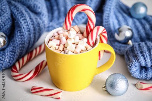Cup of tasty cocoa with marshmallows, candy canes and Christmas decor on white table
