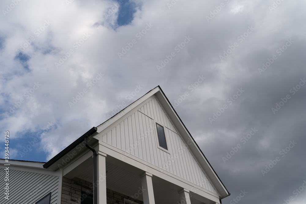Large veranda, covered porch with four white columns black metal railings, stone veneer wall cover white gable roof with elegant white vertical vinyl siding blue sky background