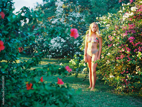 blonde teenager in bikini standing in flowering garden bushes photo
