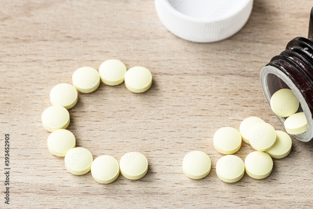 Vitamin C yellow pills and bottle on wooden background