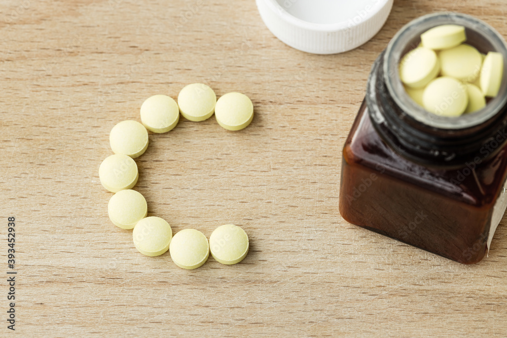 Vitamin C yellow pills and bottle on wooden background Vitamin C yellow pills and bottle on wooden background