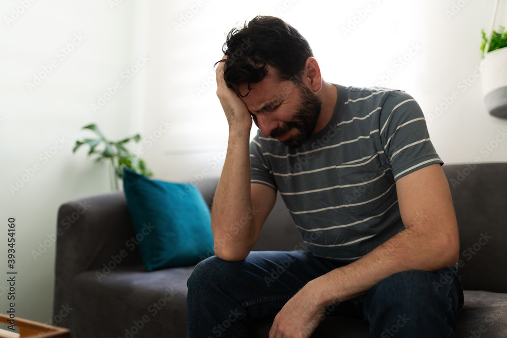 Sad adult man crying alone on the couch Sad adult man crying alone on the couch