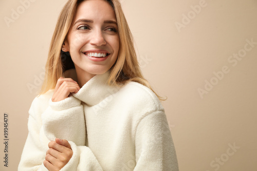Beautiful young woman wearing knitted sweater on beige background. Space for text photo