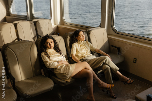 matching sisters in elegant outfits lounging in sunlight on a ferry boat