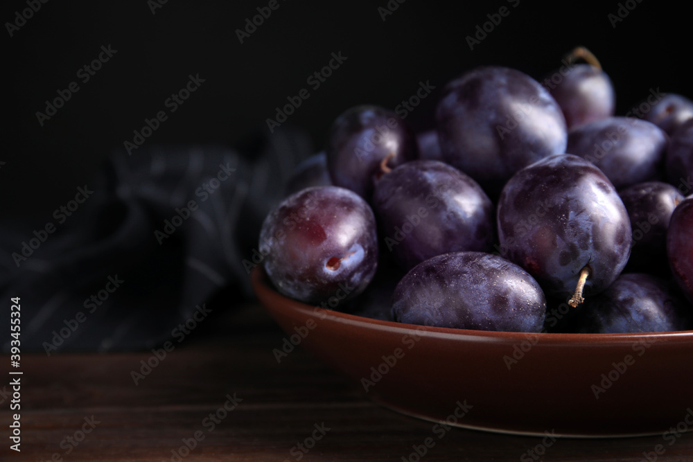Delicious ripe plums in bowl on wooden table, space for text