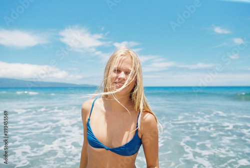 Blonde girl in blue bikini at sunshiney beach in summer with sunglasses and rainbow towel