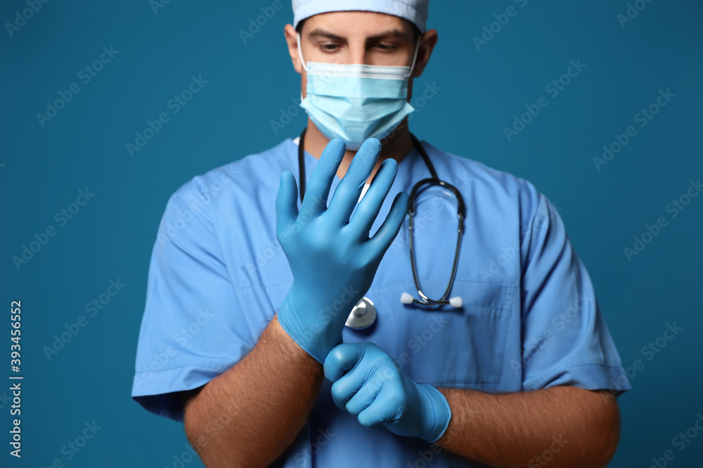 Doctor in protective mask putting on medical gloves against blue background Doctor in protective mask putting on medical gloves against blue background