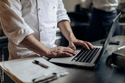 Crop chef browsing laptop in kitchen photo