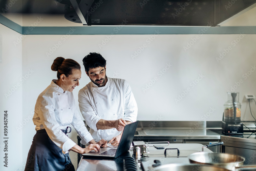 Adult chefs browsing laptop in kitchen Adult chefs browsing laptop in kitchen
