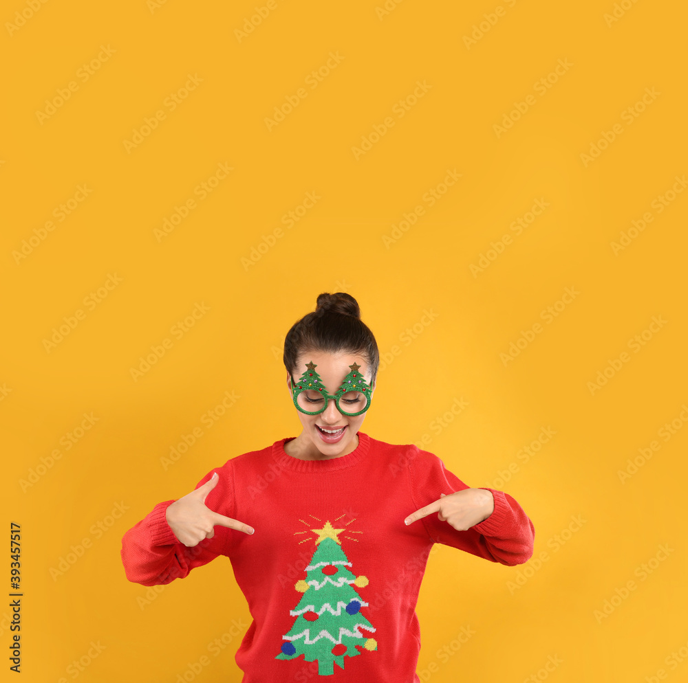 Young woman in Christmas sweater and party glasses on yellow background Young woman in Christmas sweater and party glasses on yellow background