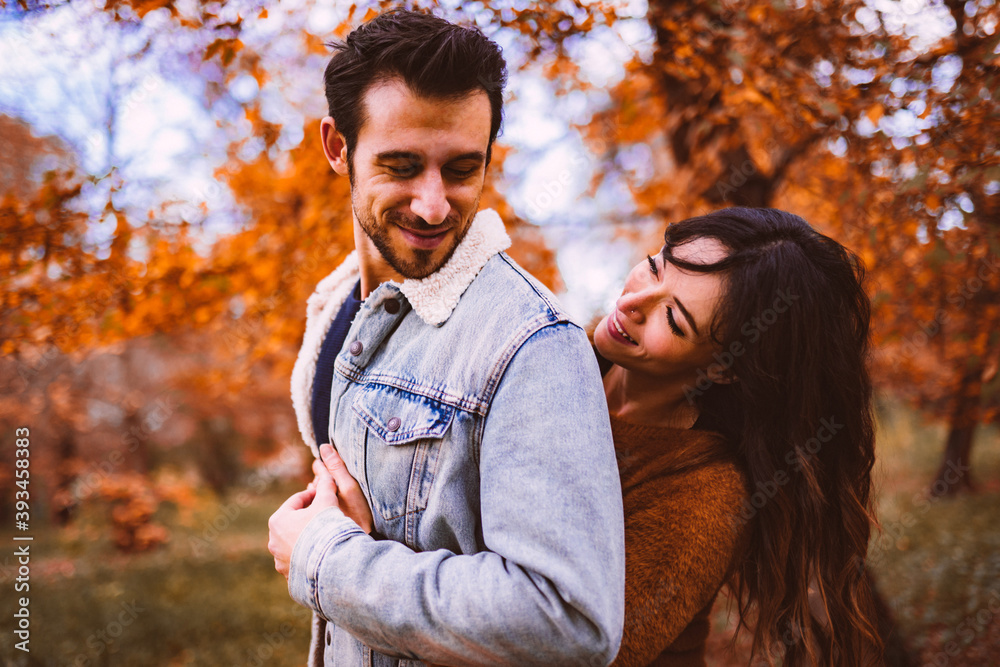 a man and a woman hugging each other in the middle of a park with autumn colors