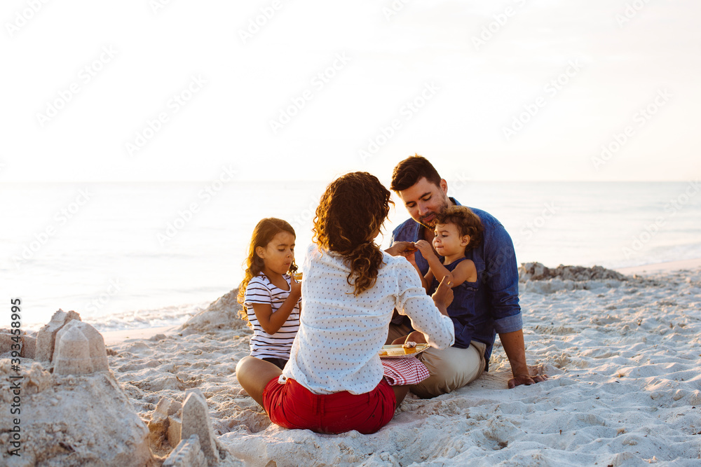 Multiracial family eating snacks on sandy beach Multiracial family eating snacks on sandy beach