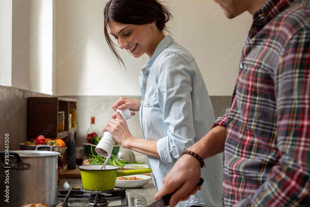 Happy woman adding spice to sauce while cooking with boyfriend Happy woman adding spice to sauce while cooking with boyfriend