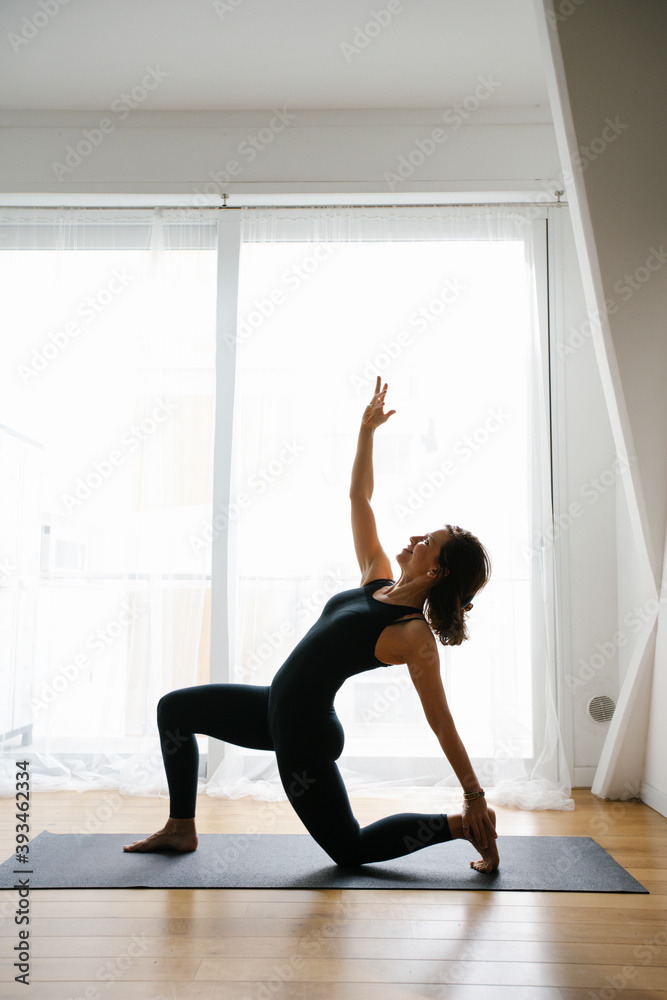 Barefooted flexible woman stretching body in standing bow pose while practicing yoga at home Barefooted flexible woman stretching body in standing bow pose while practicing yoga at home